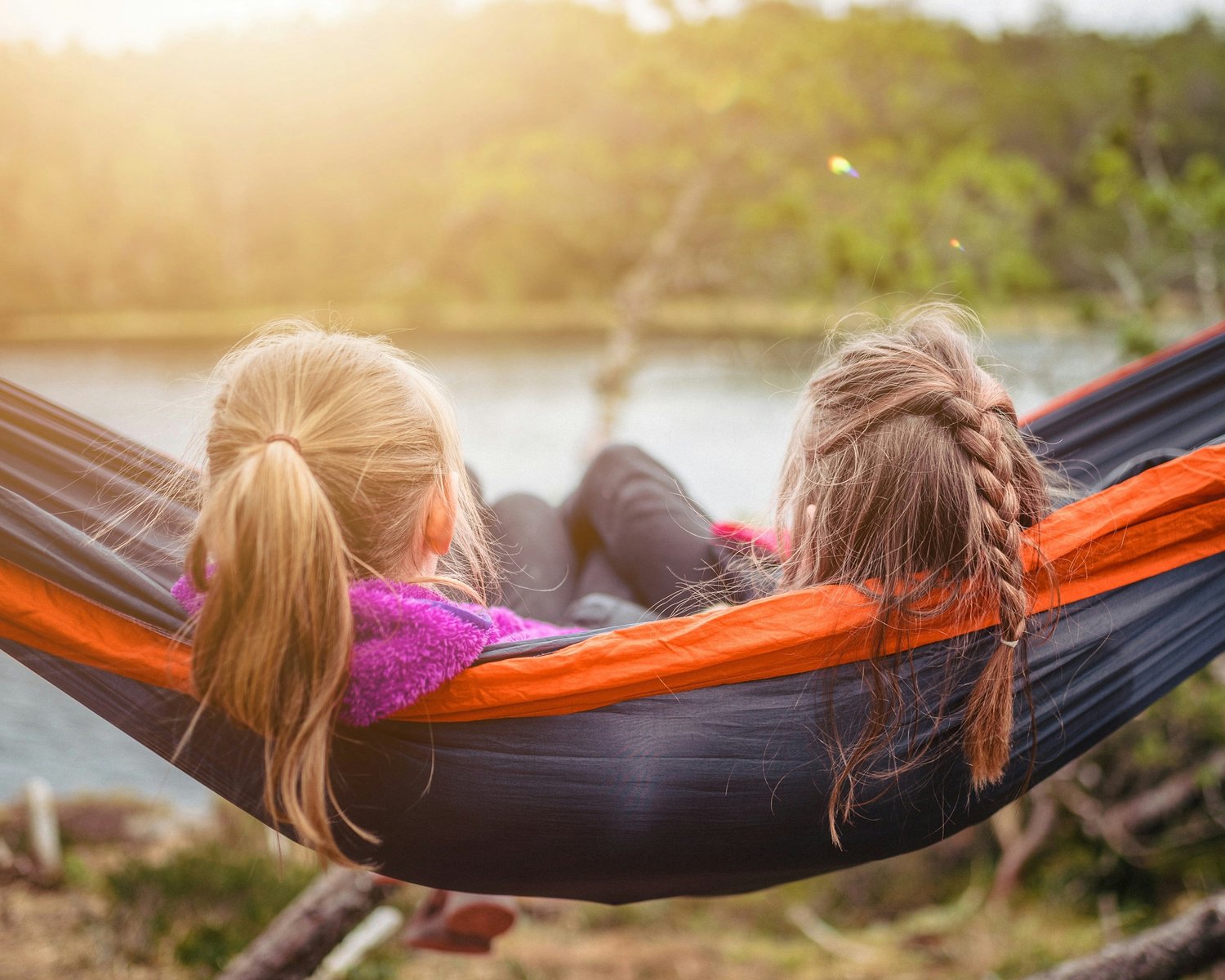 two friends sitting together in a hammock looking over water