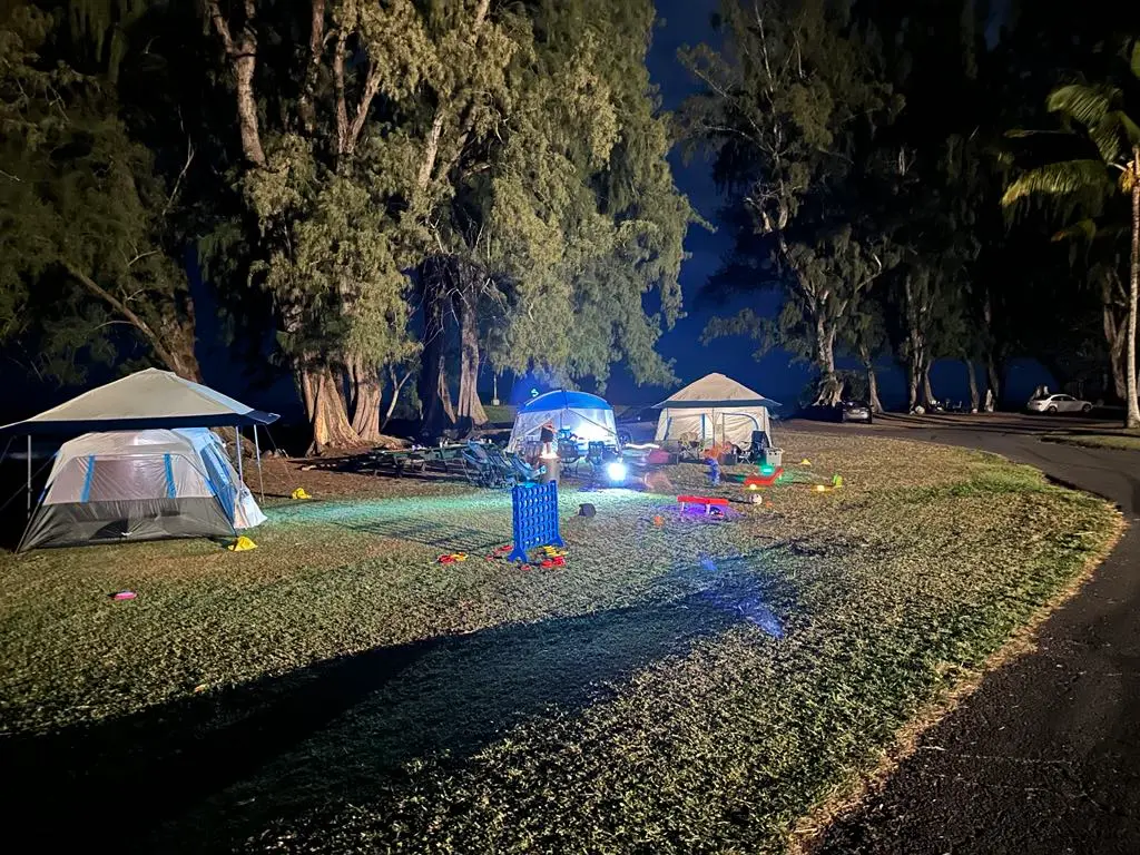 night campsite with tents, canopies, connect four game, camping chairs, bubbles, fire pit